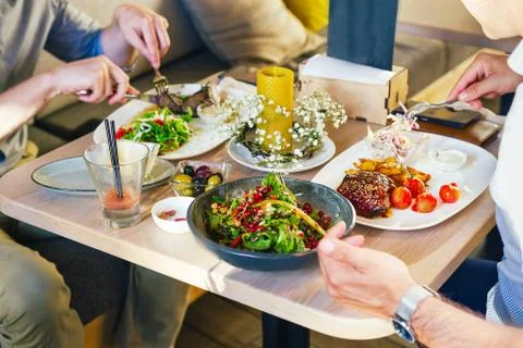 At the table, two men eat dinner, eat a steak, with a salad on a white plate, Stock Photos
