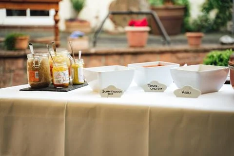 Table with various sauces and dips in glasses and white square bowls Stock Photos