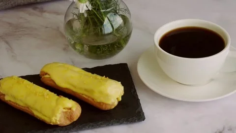 On the table is a white cup with black coffee and lemon eclairs Stock Footage 204739712