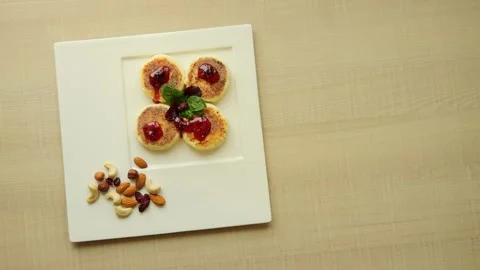 On table, white plate with freshly cooked syrniki topped with jam. Syrniki Stock Footage 264806057