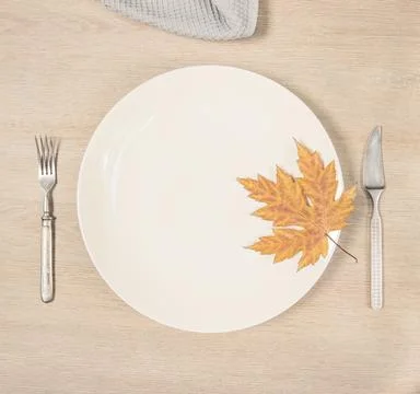 On the table is a white plate with a maple leaf, fork, knife and napkin Stock Photos
