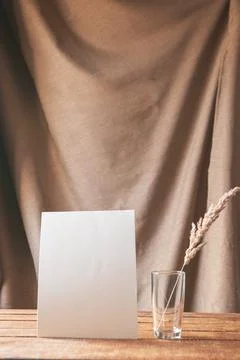 On the table is a white sheet of paper with dried flowers in a glass. Stock Photos