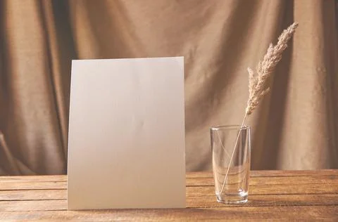 On the table is a white sheet of paper with dried flowers in a glass. Stock Photos