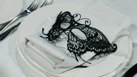 On a table with a white tablecloth is a plate with a black Venetian mask Stock Footage 122667745
