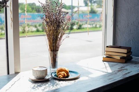 A table by the window in a cafe. A cup of coffee, a stack of books, a bouquet Stock Photos