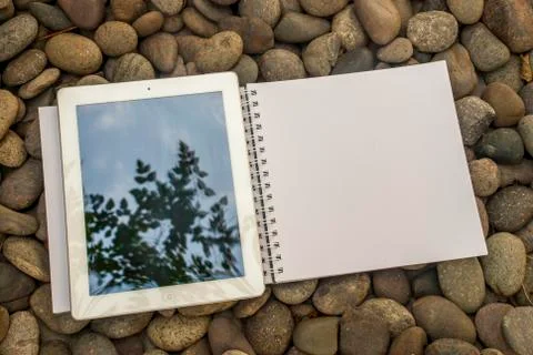 Tablet and notebook that are placed on a pile of stones Stock Photos