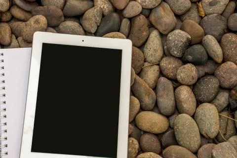 Tablet and notebook that are placed on a pile of stones Stock Photos