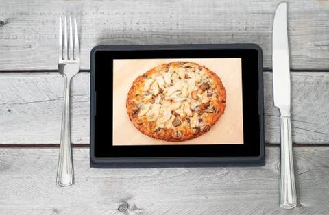 Tablet with an appetizing chicken pizza on its display between a fork and kni Foto stock