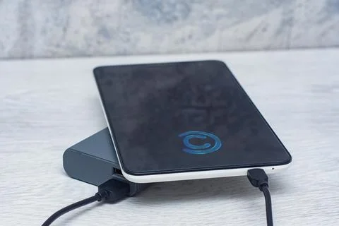 The Tablet is being charged using a portable charger on a wooden table. Stock Photos