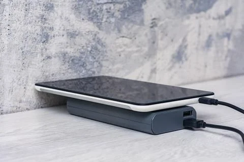 The Tablet is being charged using a portable charger on a wooden table. Stock Photos
