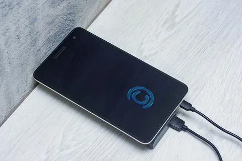 The Tablet is being charged using a portable charger on a wooden table. Stock Photos