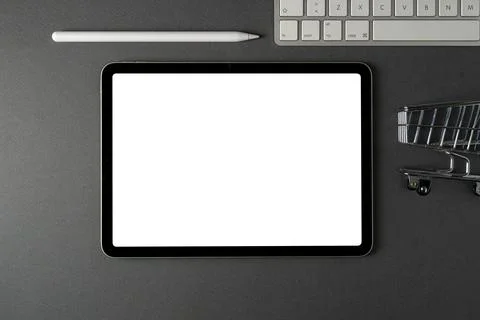 Tablet with blank screen, keyboard and supermarket cart on dark gray office.. Stock Photos