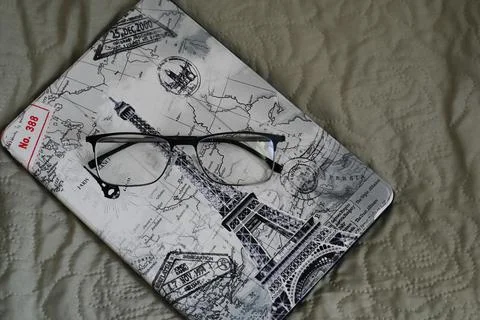 The tablet in the case is lying on the bed with glasses on it Stock Photos