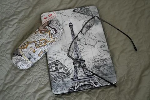 The tablet in the case is lying on the bed with glasses on it 스톡 사진