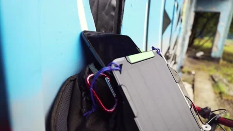 Tablet is charged from a portable solar panel battery attached to backpack. Stock-Footage 157333195