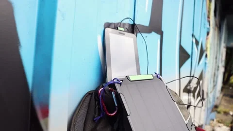 Tablet is charged from a portable solar panel battery attached to backpack. Stock Footage 157333226