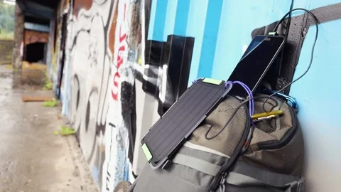 Tablet is charged from a portable solar panel battery attached to backpack. Stock Footage 157333237