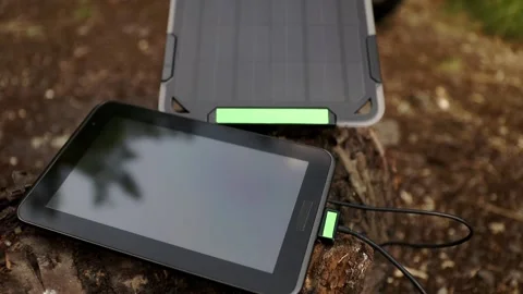 Tablet is charged from a portable solar panel on a tree stump in a forrest. Video stock 157495800