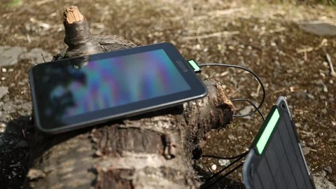 Tablet is charged from a portable solar panel on a tree stump in a forrest. Stock Footage 157495802