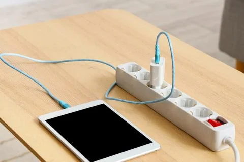 Tablet charging from a white power strip with a blue cable on a light wooden  Stock Photos