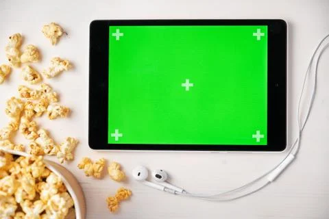 Tablet with chroma key, popcorn box and Apple earphones on the white table Stock Photos