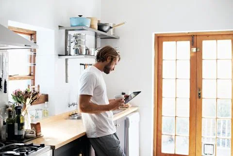 Tablet, coffee and man in kitchen for social media, online networking and Stock Photos