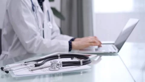Tablet computer and black stethoscope are on the glass table besides a doctor Stock Photos