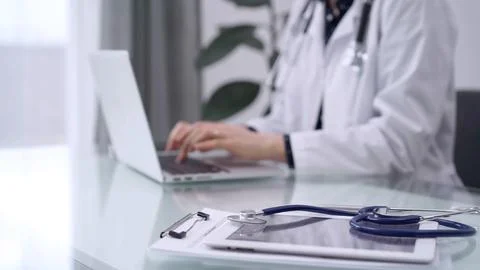 Tablet computer and blue stethoscope are on the glass table while doctor woman Stock Photos