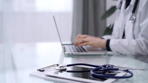 Tablet computer and blue stethoscope are on the glass table while doctor woman 스톡 사진