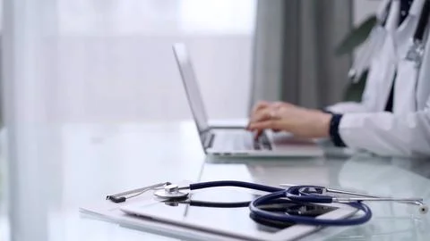Tablet computer and blue stethoscope are on the glass table while doctor woman Foto stock