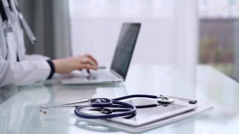 Tablet computer and blue stethoscope are on the glass table while doctor woman Stock-Fotos