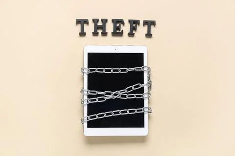 Tablet computer with chains and word THEFT on beige background Stock Photos