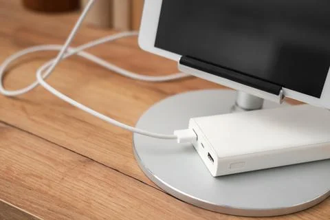 Tablet computer charging from power bank on shelf in room, closeup Stock Photos