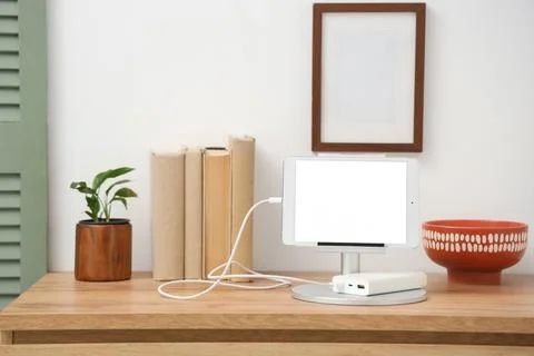 Tablet computer charging from power bank on shelf in room Stock Photos