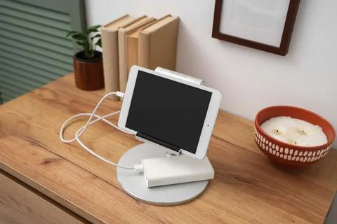 Tablet computer charging from power bank on shelf in room Stock Photos