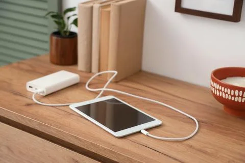 Tablet computer charging from power bank on shelf in room, closeup Stock Photos