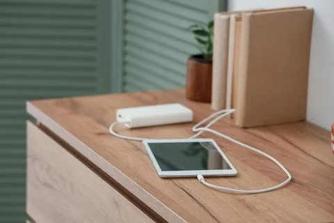 Tablet computer charging from power bank on shelf in room, closeup Stock Photos