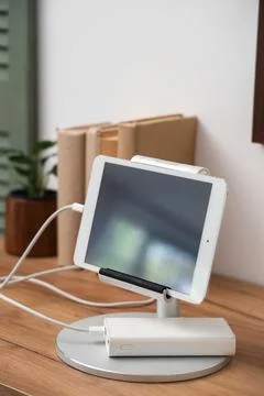 Tablet computer charging from power bank on shelf in room, closeup Stock Photos