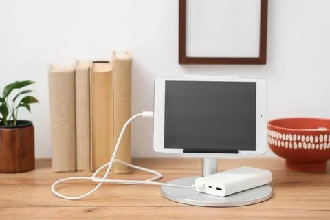 Tablet computer charging from power bank on shelf in room Stock Photos