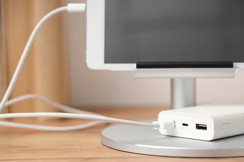 Tablet computer charging from power bank on shelf in room, closeup Stock Photos