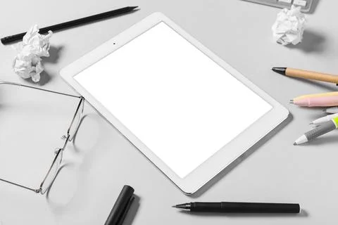 Tablet computer with crumpled paper, pens and eyeglasses on grey background Stock Photos