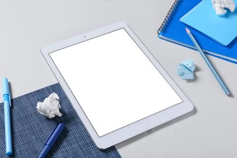 Tablet computer with crumpled paper, pens and notebooks on grey background Stock Photos