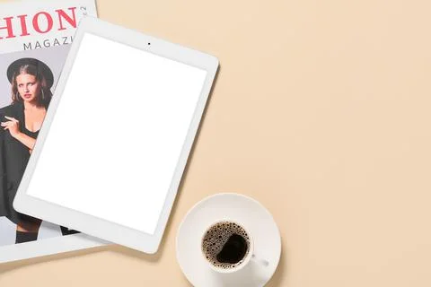 Tablet computer with cup of coffee and fashion magazine on beige background Stock Photos