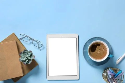 Tablet computer with cup of coffee, eyeglasses and stationery on blue backgro Stock Photos