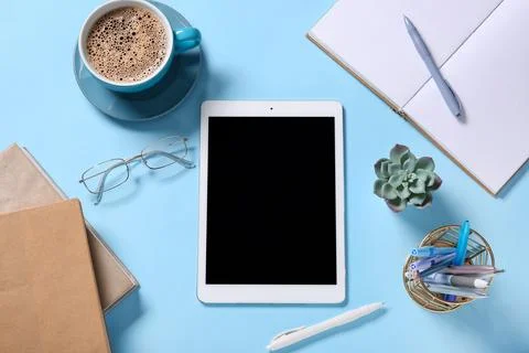Tablet computer with cup of coffee, eyeglasses and stationery on blue backgro Stock Photos