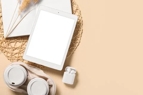 Tablet computer with earphones, takeaway cups of coffee and notebook on beige Stock Photos