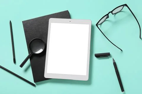 Tablet computer with notebook, eyeglasses and magnifying glass on turquoise b Stock Photos