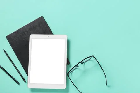 Tablet computer with notebook, eyeglasses and pencils on turquoise background Stock Photos