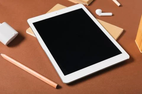 Tablet computer with notebook, pencil and earphones on brown background Stock Photos