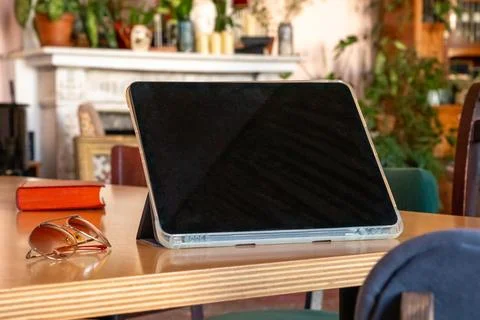 Tablet computer propped on wooden table beside book and eyeglasses in a hom.. Stock Photos